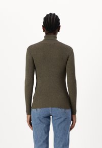 Olive green ribbed turtleneck sweater with long sleeves, fitted design, and textured fabric, paired with blue jeans.