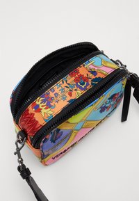 Barevná crossbody taška s květinovým vzorem na syntetickém materiálu, dvojitým zipovým uzávěrem a stříbrnými kovovými prvky, s odnímatelným popruhem.