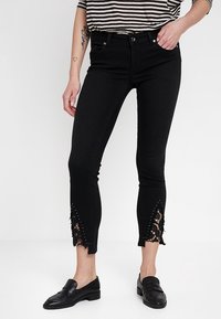 Svart slim fit jeans med spetsaccenter och nitar vid fållen. Tillverkade av denim med en figursydd design. Innehåller framfickor.