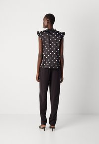 Svart bluse med prikker, ruffle-ermer og blonde detaljer ved halsen, kombinert med svarte bukser og høye mules.