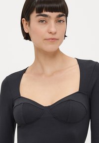 Haut noir à manches longues avec encolure carrée et détails style bustier avec coutures marquées, fabriqué dans un tissu doux et extensible.