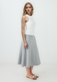 Mouwloze witte top en grijze wijde rok van zacht materiaal, met een gladde textuur en subtiele val. Gekocht met beige slide sandaaltjes.