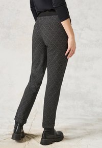 Pantaloni neri a motivo presentano un design a diamante, una vestibilità affusolata, una cintura elastica e tasche laterali, abbinati a stivaletti neri.