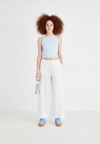 Világoskék ujjatlan blúz, fehér, széles lábú nadrág, elasztikus derékkal, kék sneakers éger talppal és ezüst kézitáska. Textúrás anyag.