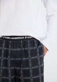 Pantaloni de lounge cu carouri negre, având un brâu cu logo-ul alb Karl Lagerfeld, prezentând o croială lejeră și un model de rețea cu linii fine.