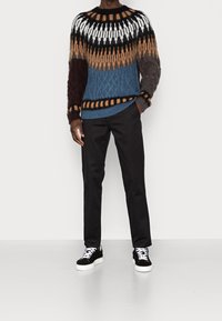 Maglione lavorato a maglia in blu, marrone e nero con motivi geometrici; abbinato a pantaloni neri e sneakers nere con lacci bianchi.