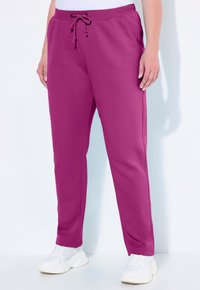 Pantaloni sportivi fucsia con cintura regolabile, tasche laterali e design con gamba affusolata, abbinati a scarpe da ginnastica bianche.