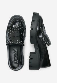 Scarpe slip-on in finta pelle lucida nera con suola spessa, frange borchiate, una fascia larga e un dettaglio testurizzato sui lati.