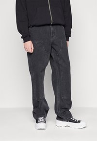 Dark denim cargo pants featuring a loose fit, multiple pockets, and contrasting stitching, paired with black and white sneakers.