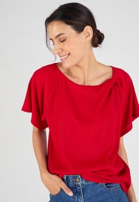 Top rosso a costine con maniche corte e dettaglio arricciato sul collo, abbinato a jeans in denim blu.