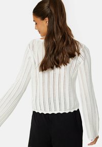 Weißer Strickpullover mit vertikalem Rippenmuster, lockerer Passform, gewelltem Saum und langen Ärmeln. Leichte Textur, geeignet zum Layering.