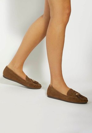 Brown suede loafers with a rounded toe, featuring a decorative tassel and gold-tone hardware accents. Flat sole design for easy wear.