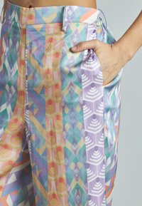Pantalons colorés à motifs avec des designs géométriques dans des tons de rose, violet, bleu et jaune, avec un détail de poche latérale.