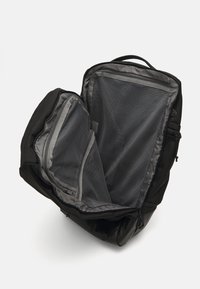 Sac à dos noir avec des poches intérieures en mesh ; doté d'un design profilé et arrondi, ainsi que d'une poignée supérieure pour un transport facile. Fermetures à glissière visibles.