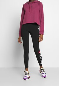 Sudadera acanalada burdeos con bolsillo frontal, leggings negros con texto blanco y zapatillas multicolor con suela gruesa y cordones.