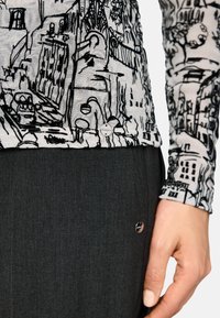 Langärmliges Oberteil mit einer monochromatischen Gebäudeillustration auf hellem Hintergrund, kombiniert mit einem dunkelgrauen Rock, der ein kreisförmiges metallisches Akzent besitzt.