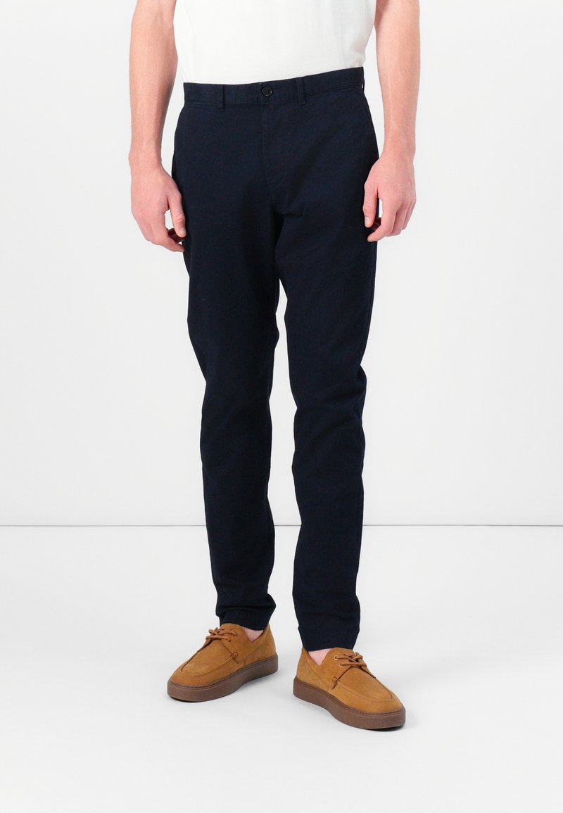 Chinos bleu marine en coton mélangé, avec une coupe slim, des poches avant, une fermeture avec bouton et associés à des chaussures en daim tan.