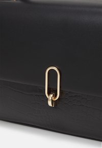 Sac à main noir avec des sections en simili cuir lisse et texturé et une fermeture ovale dorée sur le rabat avant.