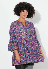 Tunika floreale multicolore in viola, con scollatura a V, orlo a strati e maniche a campana. Il tessuto sembra leggero con un design fluido.