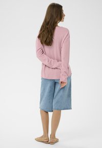 Haut rose à manches longues, short en denim ample et sandales tissées de couleur claire. Texture douce et design décontracté, vue de dos.