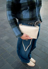 Crème kleurige leren clutch met reliëf stippen, zilveren ritssluiting accenten en verstelbare riem, gecombineerd met een blauwgroene geruite wollen trui en spijkerbroek.