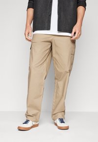 Beige cargo pants with a relaxed fit, made of lightweight fabric, featuring side pockets and a smooth surface texture. Paired with white shoes.