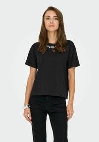 Zwarte t-shirt met korte mouwen en een ronde halslijn, voorzien van een bloemenversiering bij de kraag. Soepele katoen stof, ontspannen pasvorm.