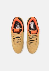 Barna suéd sneaker fekete és narancssárga részletekkel. Jellemzői a párnázott nyak, perforált orr és lapos fekete cipőfűző. Márkajelzés a talpbetétekön.