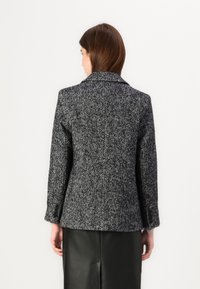 Blazer à motif pied-de-coq noir et blanc avec un col cranté et un détail de bouton unique, associé à une jupe en cuir noire.