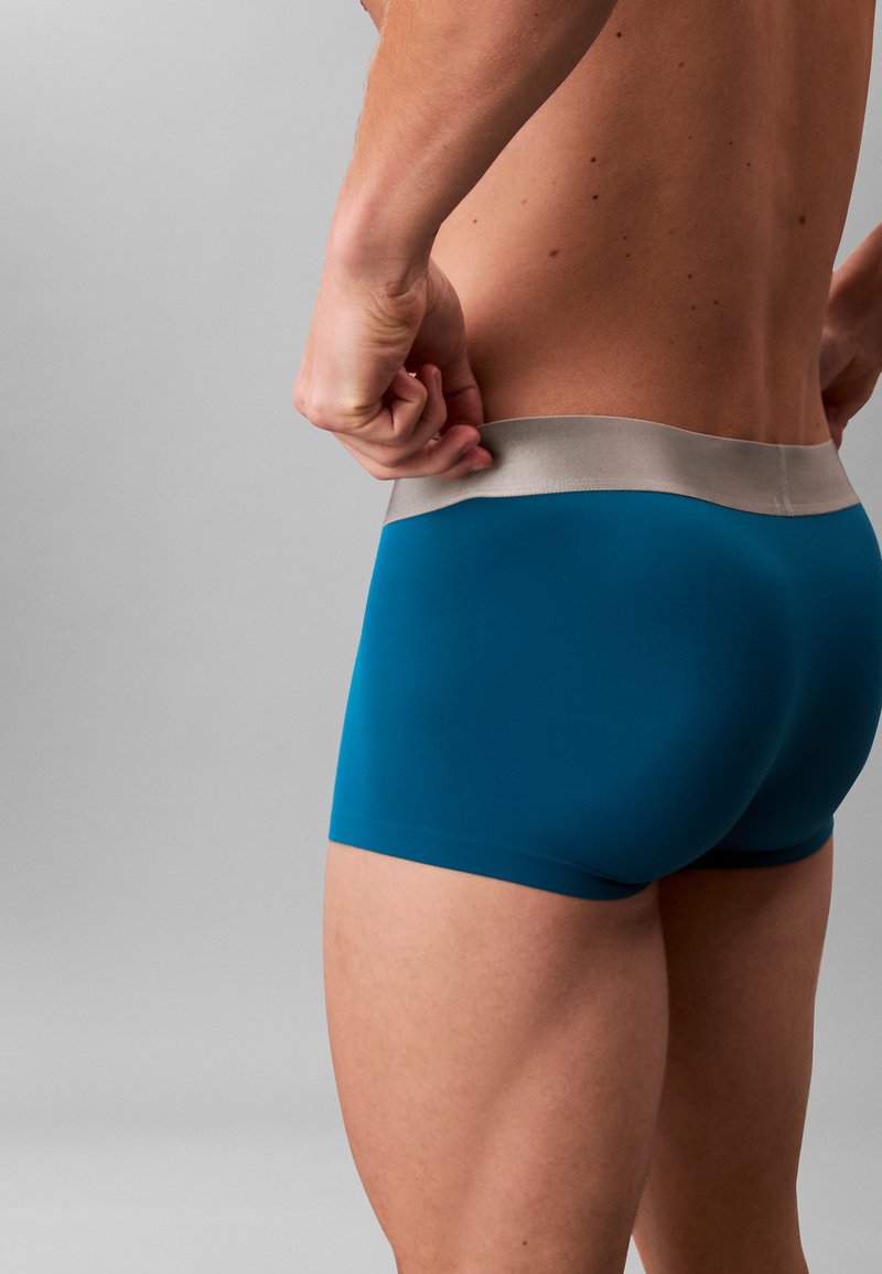 Boxers pour hommes de couleur sarcelle avec une ceinture grise. Matière douce et extensible avec une finition lisse. La coupe met en valeur les jambes et la taille.