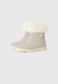 Beiga ankelstövlar i slätt material, med en fluffig vit krage och ett hjärtformat accent. Sulan är ljusfärgad med ett strukturerat mönster.