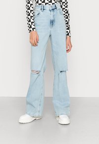 Jeans de perna larga azul claro com detalhes de joelho rasgado e cintura alta. Feitos de denim, apresentam um design clássico de cinco bolsos.