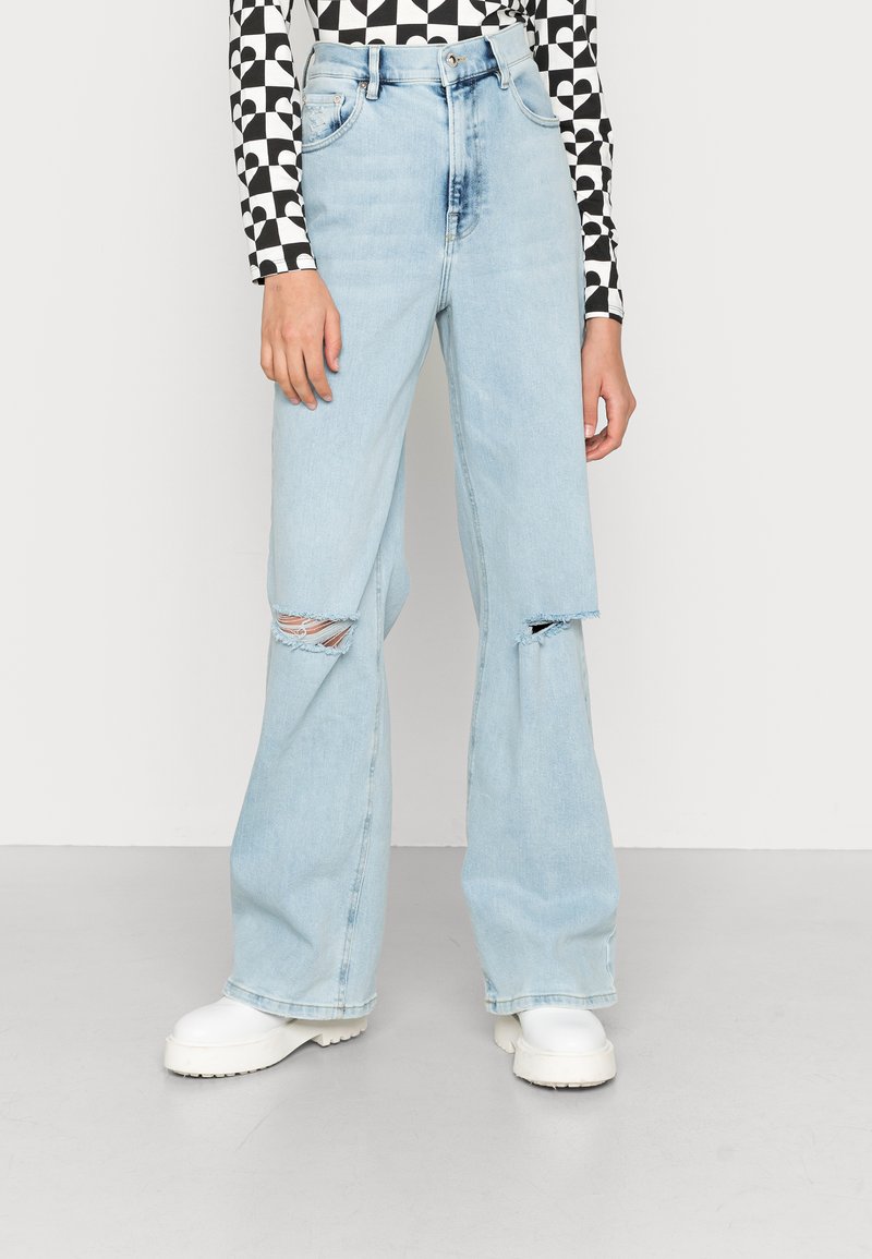 Jeans de perna larga azul claro com detalhes de joelho rasgado e cintura alta. Feitos de denim, apresentam um design clássico de cinco bolsos.