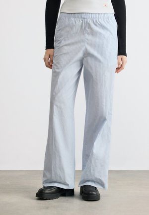 Pantalon large à rayures fines bleu clair avec taille élastique, porté avec des chaussures noires épaisses et un haut noir à manches longues.