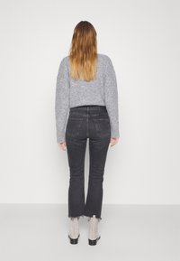 Suéter gris de punto, jeans negros de cintura alta con corte acampanado, y botas de ante gris con tacón ancho. Diseño y texturas simples.