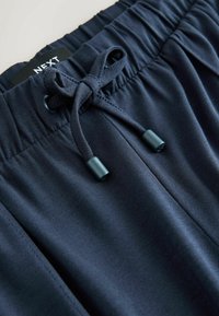 Marineblaue Shorts aus einem glatten Material mit elastischem Bund und verstellbarem Kordelzug. Die Kordel hat metallische Spitzen.