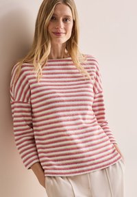 Top de punto con rayas horizontales rojas y blancas, escote barco, mangas de tres cuartos y un corte holgado, combinado con pantalones claros.