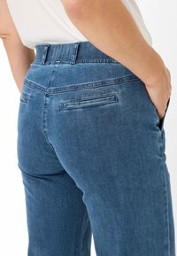 Jeans i mellemblå med en glat tekstur. Har høj talje, baglommer og bæltestropper. Tilpasset pasform med et klassisk design.