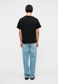 Μαύρο βαμβακερό T-shirt μ ε κοντά μανίκια και στρογγυλή λαιμόκοψη, σε συνδυασμό με ανοιχτόχρωμο τζιν παντελόνι, με άνετη εφαρμογή και ορατές ραφές.