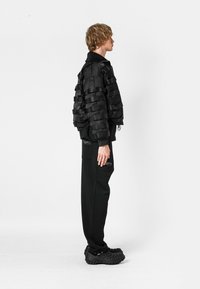 Chaqueta negra corta con paneles texturizados en capas, combinada con pantalones negros con bolsillos. El calzado es grueso, negro y perforado.