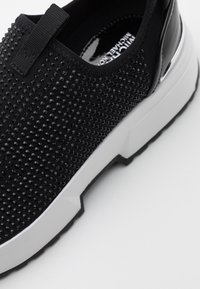 Černé slip-on tenisky s texturovaným svrškem a vystouplými hroty, elastickými boky a bílou robustní podrážkou. Hladké lakované akcenty na patě.