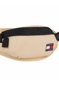 Bolso de cintura de tela beige con correa negra, que presenta un parche con el logo "TOMMY JEANS". Diseño sencillo con una textura suave y cierre ajustable.