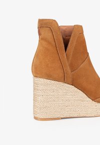 Bottine à talon compensé en suède marron avec une semelle en corde texturée, présentant un design en forme de V à la cheville et des détails de couture minimalistes.