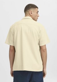 Beige shirt met korte mouwen van een textuurstof, met een kraag en een ontspannen pasvorm. De zoom is recht en komt tot de taille.