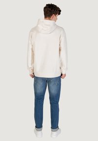 Crème kleurige hoodie met een trekkoordcapuchon, een relaxte pasvorm, geribbelde manchetten en zoom, gecombineerd met blauwe jeans en witte sneakers.