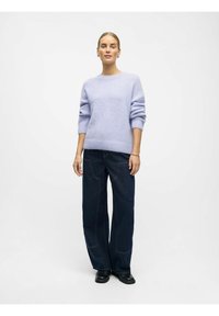 Maglione lavorato a maglia colore lilla chiaro con maniche arrotolate, abbinato a jeans a gamba larga blu scuro con tasche frontali e cuciture evidenti.