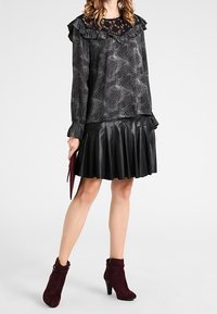 Blusa nera con yoke in pizzo e scollo arricciato, abbinata a una gonna plissettata nera in similpelle. Stivaletti borgogna con tacco alto.