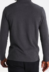 Långärmad, mörkgrå polo med mjukt tyg, med krage och sidslitsar vid fållen för ökad rörelsefrihet.