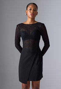 Top din dantelă neagră cu mâneci lungi și material transparent, cu un sutien pe dedesubt, asortat cu o fustă neagră tip wrap, cu o fixare la talie.
