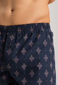 Boxer in blu navy con motivo, dotati di elastico in vita e coulisse, caratterizzati da un design floreale in rosa e bianco, realizzati in tessuto morbido con una texture liscia.